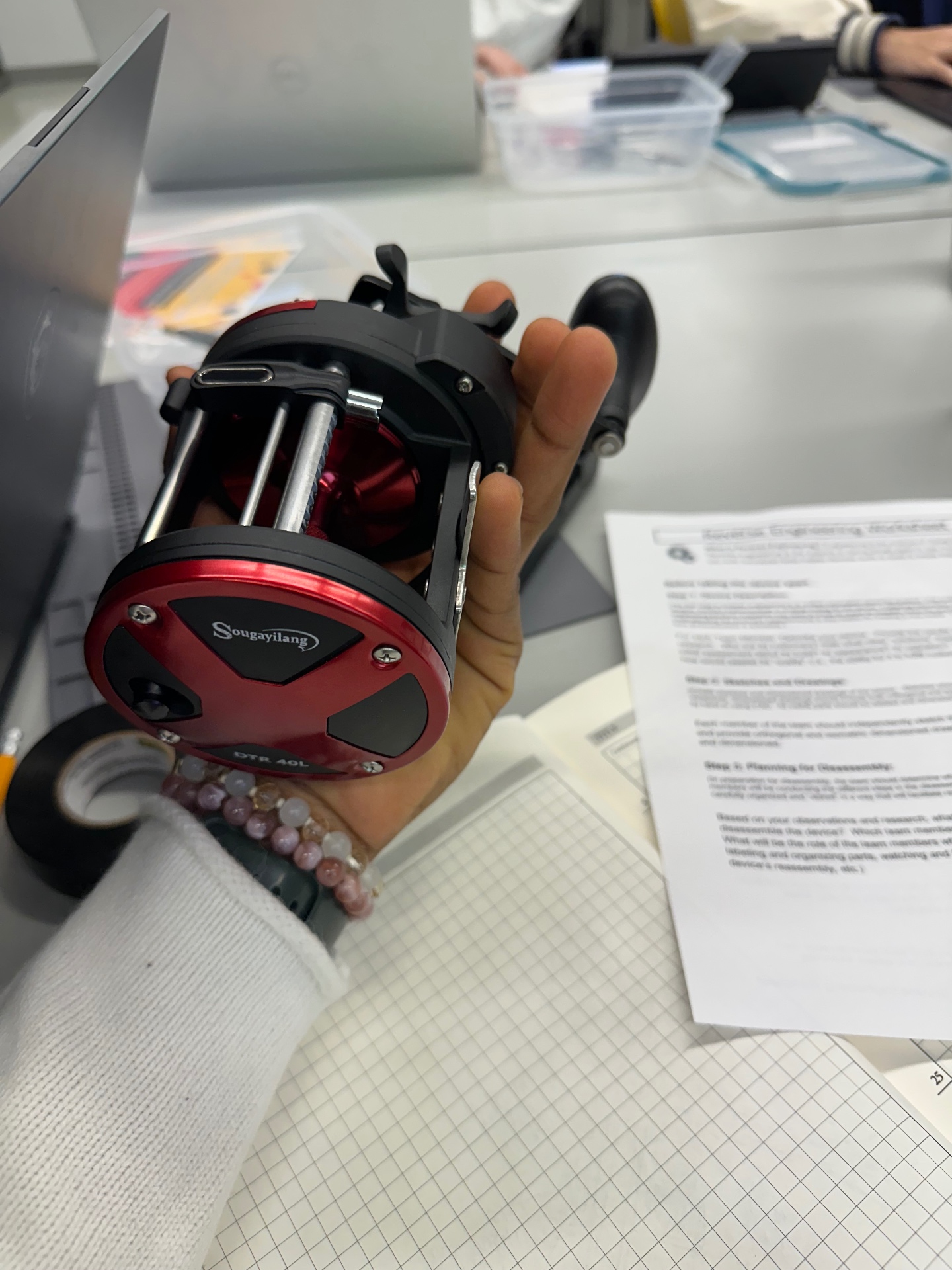 Red-and-black Sougayilang DTR 40L conventional fishing reel held in hand during the reverse-engineering teardown.