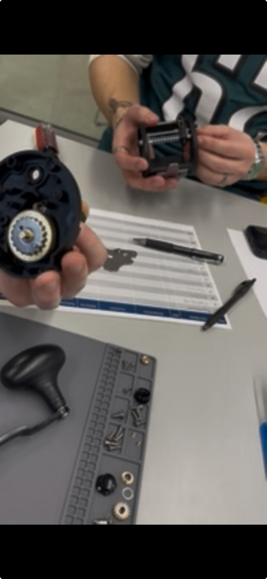 Reel side plate and internal spool/gear assembly separated during teardown, with sorted hardware tray below.