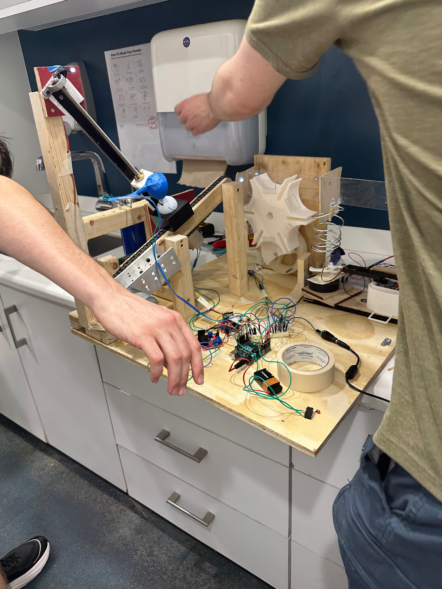 Wood-framed belt-driven golf-ball transport mechanism wired to an Arduino on a plywood test bench.